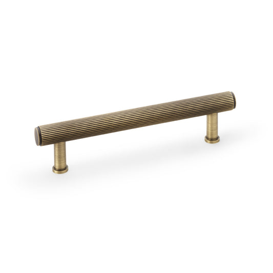 Alexander & Wilks Crispin Reeded T-bar Cupboard Pull Handle in Antique Brass, 128mm, showing detailed texture and ergonomic design.
